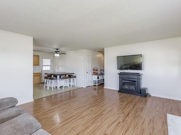 living room featuring light wood-style flooring, a textured ceiling, a fireplace, baseboards, and ceiling fan