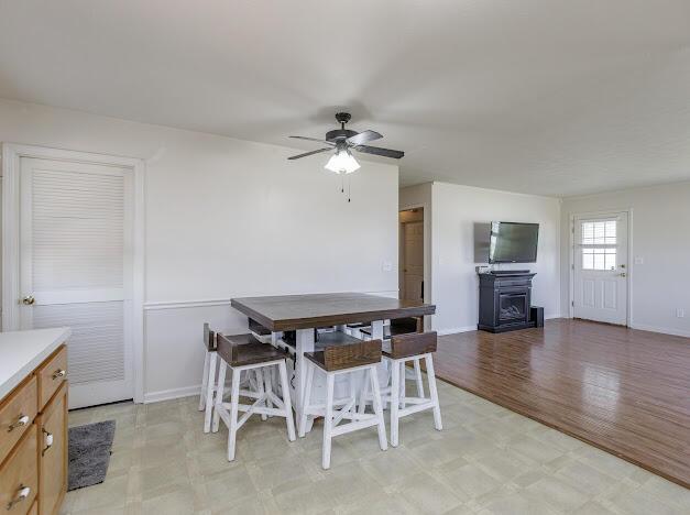 dining room featuring light floors, a fireplace, baseboards, and ceiling fan