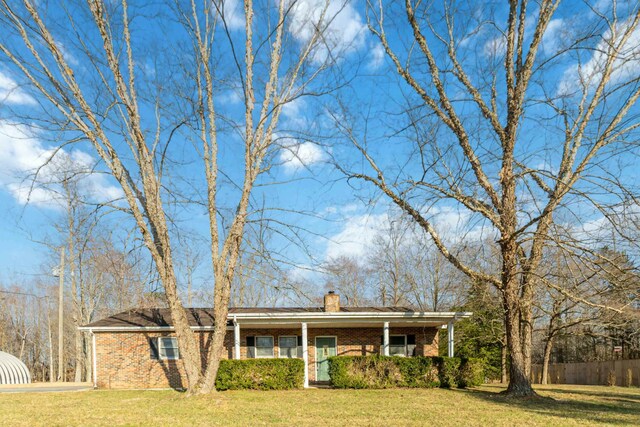 single story home with a porch, fence, a front yard, brick siding, and a chimney