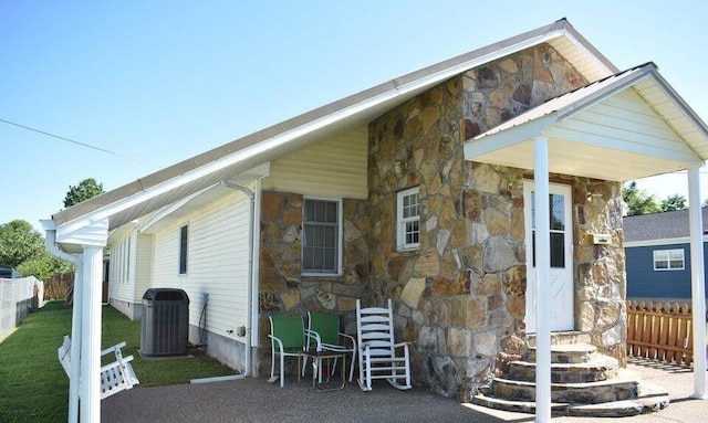 exterior space featuring fence, stone siding, and central AC