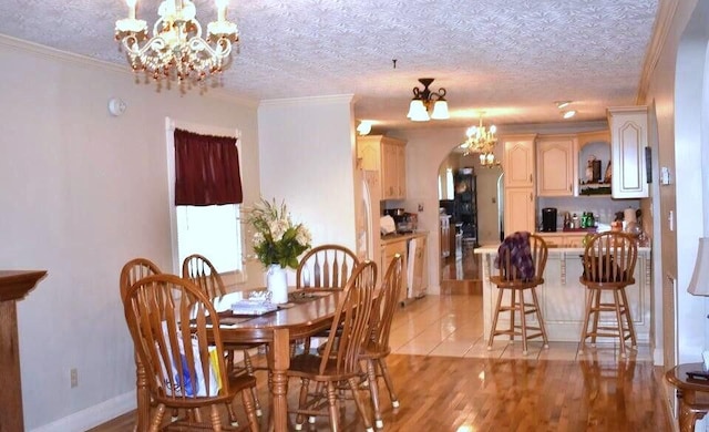 dining area featuring arched walkways, ornamental molding, a textured ceiling, a notable chandelier, and light wood-type flooring