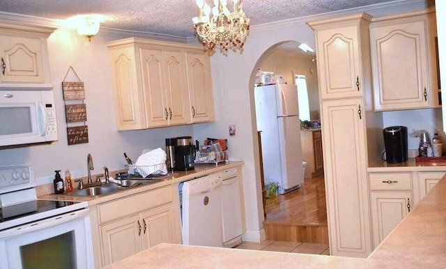 kitchen featuring cream cabinetry, a sink, white appliances, arched walkways, and crown molding