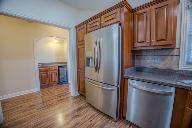 kitchen with dark countertops, wood finished floors, beverage cooler, and appliances with stainless steel finishes