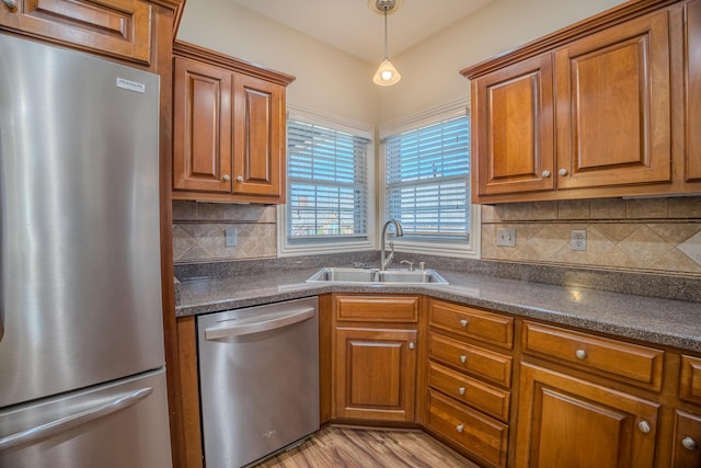 kitchen featuring dark countertops, stainless steel appliances, brown cabinetry, and a sink