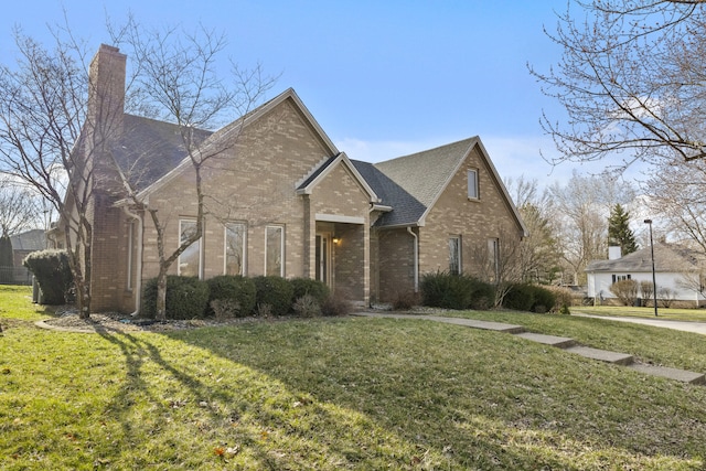 view of front of property featuring brick siding, a chimney, a front lawn, and roof with shingles