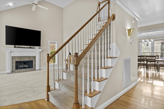 staircase featuring wood finished floors, visible vents, baseboards, a tiled fireplace, and ceiling fan with notable chandelier