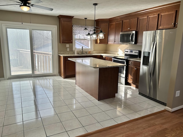 kitchen with a sink, a kitchen island, appliances with stainless steel finishes, light tile patterned floors, and ceiling fan