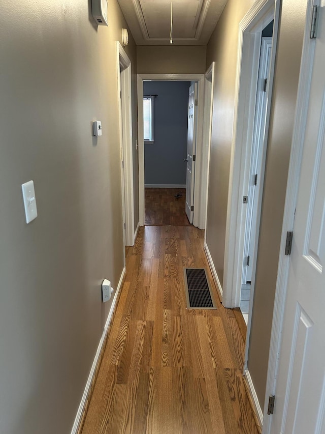 hall with light wood finished floors, visible vents, attic access, and baseboards