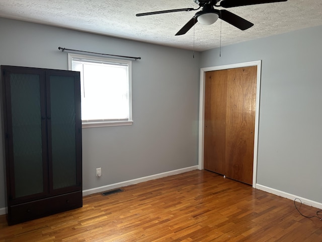 unfurnished bedroom featuring visible vents, baseboards, a textured ceiling, and wood finished floors