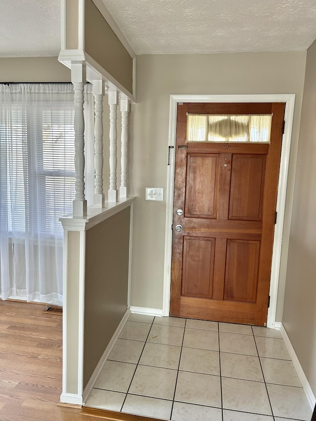 entrance foyer with light tile patterned floors, baseboards, a textured ceiling, and a healthy amount of sunlight