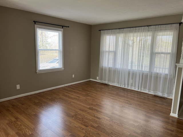 spare room with dark wood-type flooring, visible vents, and baseboards