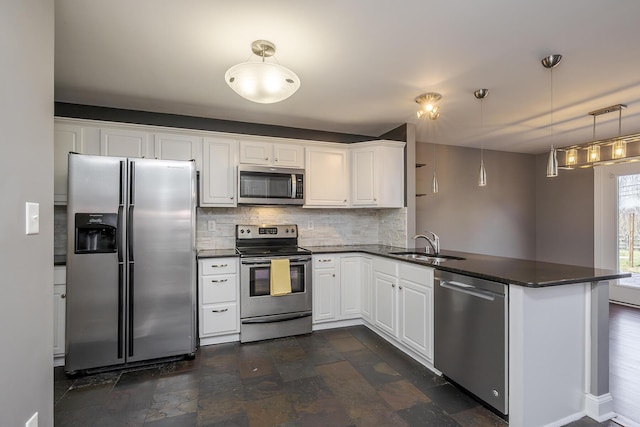 kitchen featuring dark countertops, tasteful backsplash, appliances with stainless steel finishes, a peninsula, and a sink