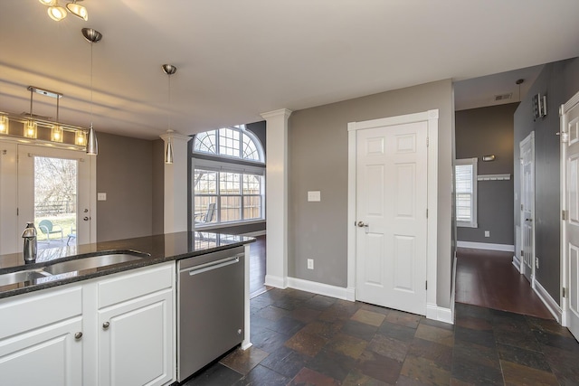 kitchen featuring dark stone countertops, stone tile floors, a sink, white cabinets, and stainless steel dishwasher