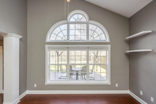 interior space featuring dark wood finished floors, a high ceiling, baseboards, and decorative columns