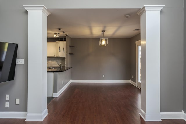 unfurnished living room with visible vents, baseboards, dark wood-type flooring, and ornate columns