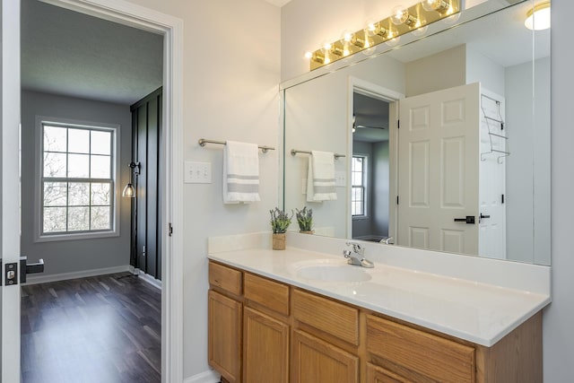 bathroom with ceiling fan, vanity, baseboards, and wood finished floors