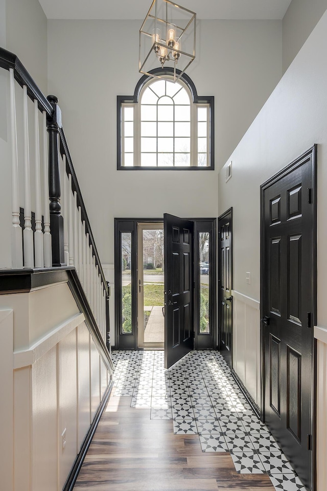 foyer featuring wood finished floors, a wainscoted wall, visible vents, an inviting chandelier, and stairs