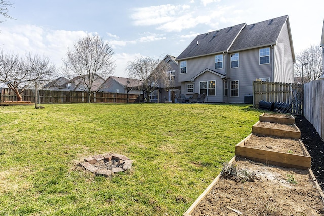 rear view of property featuring a fenced backyard, a lawn, an outdoor fire pit, and a vegetable garden