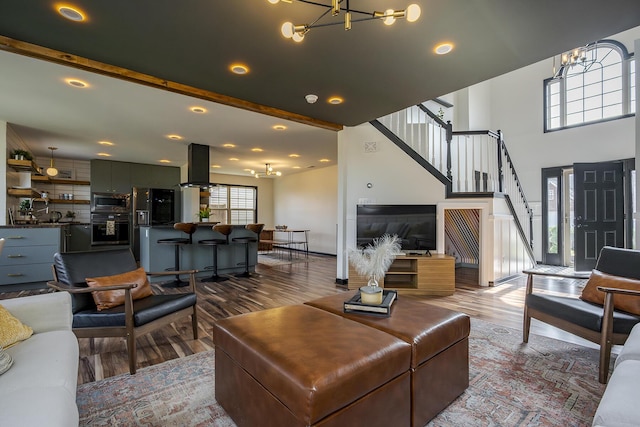 living area featuring an inviting chandelier, stairway, wood finished floors, and beamed ceiling