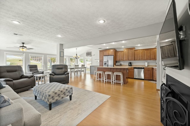 living room with visible vents, recessed lighting, light wood-style flooring, ceiling fan with notable chandelier, and a textured ceiling