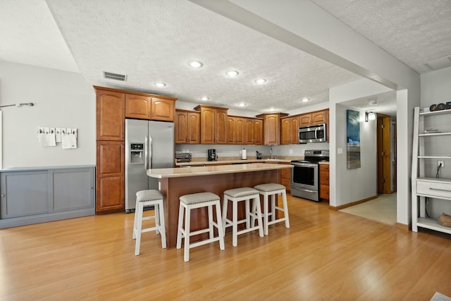 kitchen featuring a kitchen bar, visible vents, light wood-style flooring, a kitchen island, and stainless steel appliances