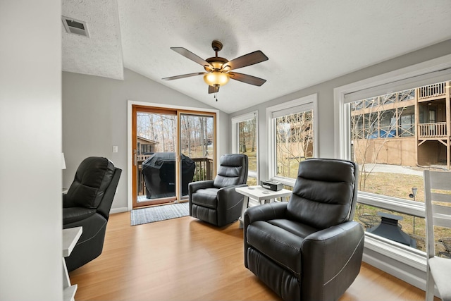 living area with wood finished floors, visible vents, ceiling fan, vaulted ceiling, and a textured ceiling