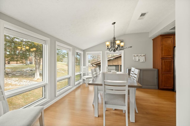 dining area featuring vaulted ceiling, light wood-style flooring, visible vents, and a chandelier