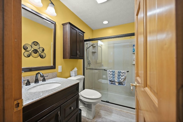 bathroom with vanity, a shower stall, toilet, and a textured ceiling