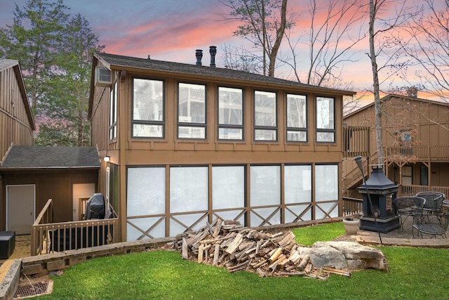 back of house at dusk with a yard, roof with shingles, and a wall unit AC