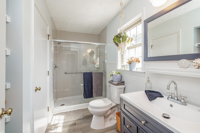 bathroom with a wainscoted wall, toilet, a stall shower, and a textured ceiling