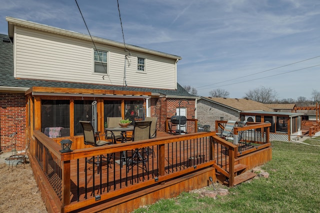 rear view of property featuring a deck, a sunroom, brick siding, and roof with shingles