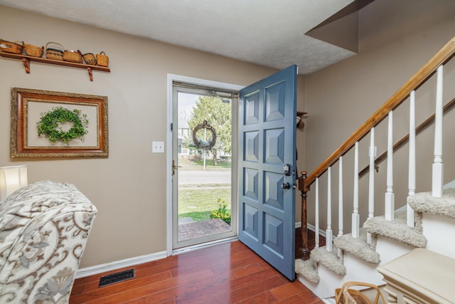 entrance foyer with wood finished floors, baseboards, visible vents, stairs, and a textured ceiling