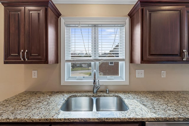 kitchen with a sink, light stone counters, and dark brown cabinets