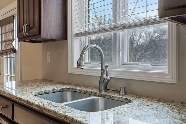 interior details featuring a sink, light stone counters, and dark brown cabinetry