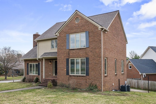 traditional-style home with fence, roof with shingles, a front yard, brick siding, and a chimney