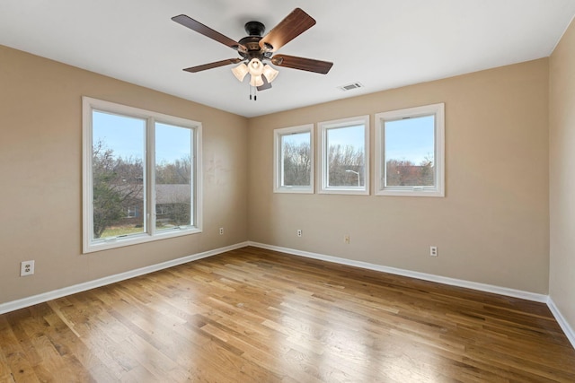 empty room featuring a ceiling fan, wood finished floors, visible vents, and baseboards