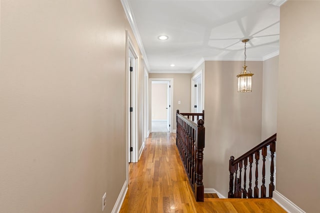 hall with an upstairs landing, light wood finished floors, crown molding, and baseboards