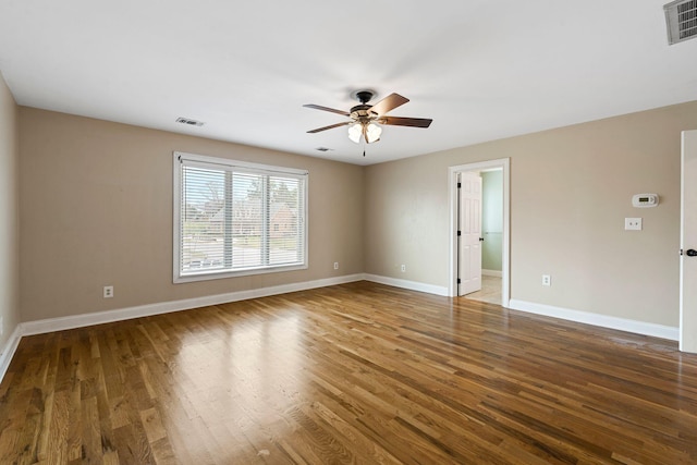empty room with wood finished floors, baseboards, a ceiling fan, and visible vents