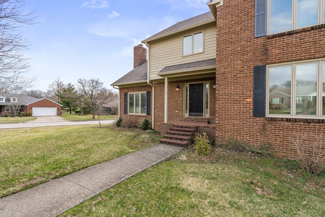 view of front of home featuring a front lawn, an outdoor structure, a shingled roof, brick siding, and a chimney