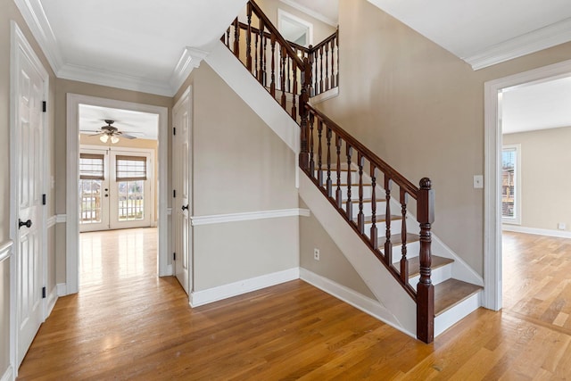 stairway featuring wood finished floors, crown molding, a healthy amount of sunlight, and baseboards