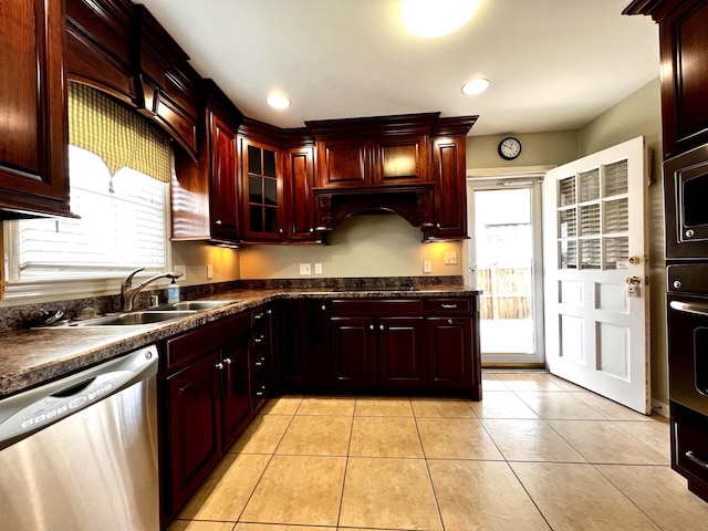 kitchen with a sink, dark countertops, reddish brown cabinets, appliances with stainless steel finishes, and light tile patterned floors