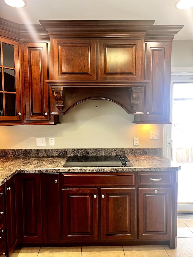 kitchen featuring glass insert cabinets, dark countertops, light tile patterned floors, black electric cooktop, and dark brown cabinets