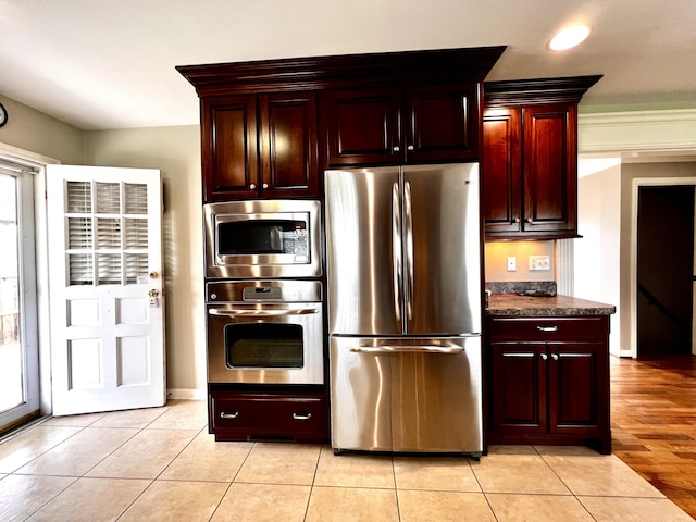 kitchen featuring light tile patterned floors, baseboards, appliances with stainless steel finishes, dark countertops, and reddish brown cabinets