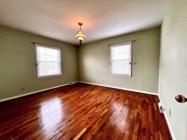 empty room with dark wood-style floors, visible vents, and baseboards