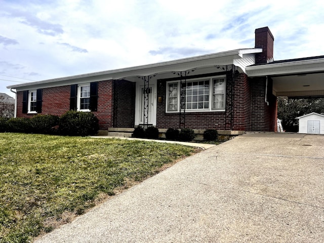 ranch-style house featuring brick siding, a carport, a front yard, an outbuilding, and driveway