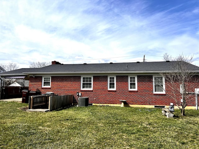 rear view of house with brick siding, an attached carport, central AC, and a yard