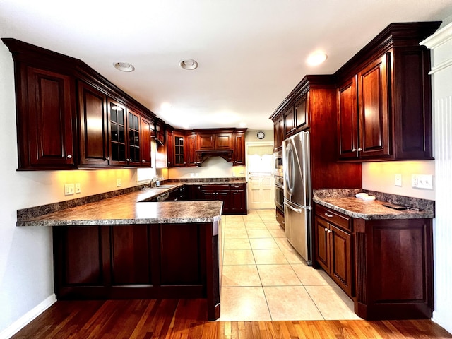 kitchen featuring a sink, dark countertops, freestanding refrigerator, a peninsula, and glass insert cabinets