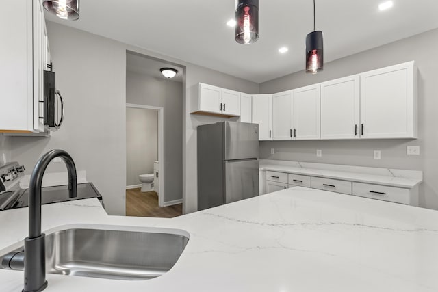 kitchen with a sink, freestanding refrigerator, white cabinets, light stone countertops, and hanging light fixtures