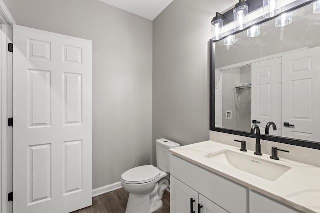 half bathroom with toilet, vanity, baseboards, and wood finished floors