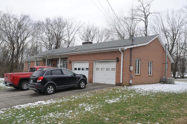 exterior space featuring cooling unit, driveway, an attached garage, a chimney, and brick siding